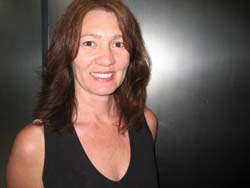 A woman with wavy brown hair smiling while wearing a black sleeveless top.