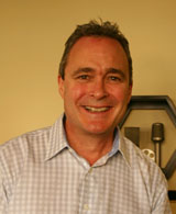 A smiling man with short hair wearing a light-colored checkered button-down shirt.