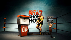 A muscular man in yellow and black athletic wear stands in a boxing ring next to a gas pump.