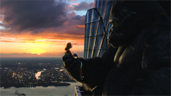 A massive gorilla holds a small woman in its hand overlooking a city at sunset.