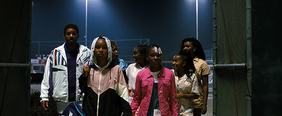 A group of people walking through a doorway toward the camera at night under bright stadium lights.
