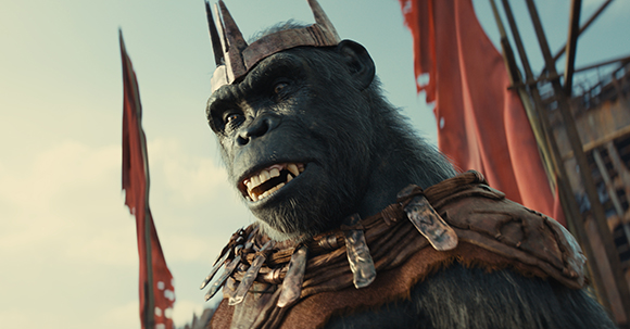 A close-up of a large ape wearing a metal crown and decorative leather armor against a sky with red flags.