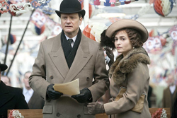 A man in a brown coat and bowler hat holds a paper next to a woman in a tan coat and wide-brimmed hat.