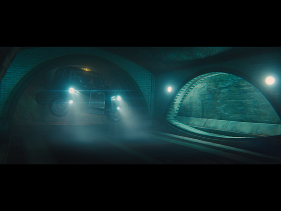 A dark vehicle with bright headlights driving through a dimly lit, arched tunnel.