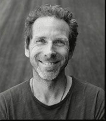 Black and white headshot of a middle-aged man with wavy hair and a slight beard, smiling at the camera.