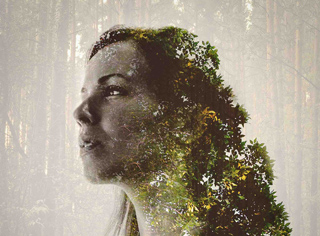Double exposure portrait of a woman's profile blended with lush green forest foliage and trees.