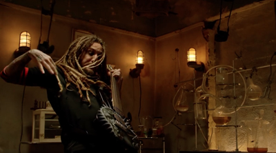A person with long dreadlocks playing an electric guitar in a dark, laboratory-like setting.