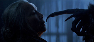 A woman in profile looks toward a dark, long-fingered clawed hand in a dimly lit blue setting.