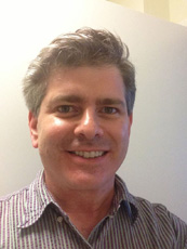 A smiling man with salt-and-pepper hair wearing a purple and white striped button-down shirt.