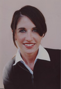 A smiling woman with dark hair wearing a black zip-up sweater over a white collared shirt.