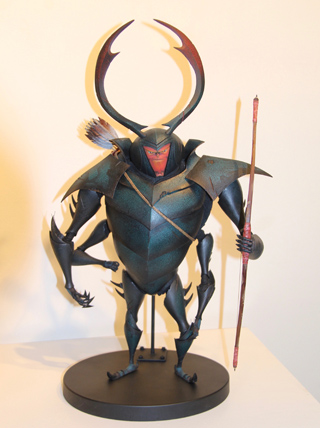 A detailed figurine of a beetle-like warrior with large curved horns, armor, and holding a bow and arrow. It stands on a blac