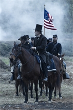 Men in 19th-century clothing riding horses through smoke, one man wearing a top hat.