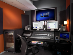 A professional audio mixing desk with multiple monitors, studio speakers, and an ergonomic chair in a dark studio.