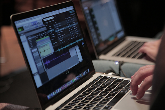 Close-up of hands typing on a laptop displaying audio editing software waveforms.