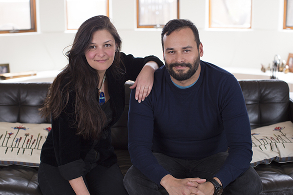 A man in a blue sweater and a woman in a black top sit together on a dark leather couch.