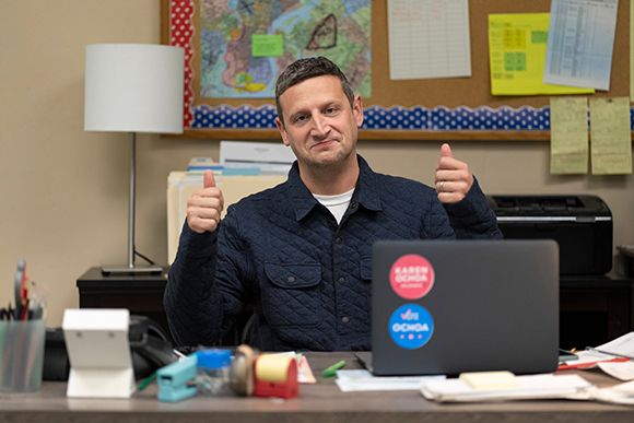 A man sitting at a desk giving two thumbs up in an office setting.