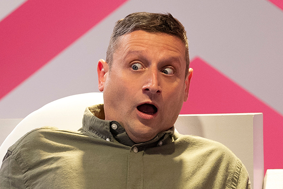 A man in a green button-down shirt looks to the side with wide eyes and an open mouth.