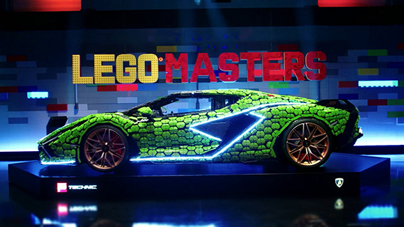 A green LEGO sports car model on a dark stage with a large LEGO Masters sign behind it.