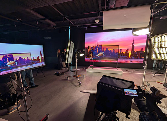 A film studio featuring large LED screens showing a sunset skyline, surrounded by lighting and camera equipment.