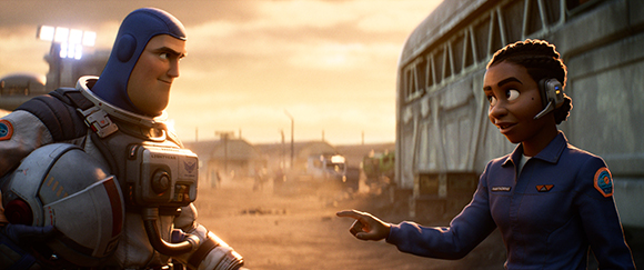 An astronaut in a white suit looks at a woman in a blue jumpsuit pointing at him in a dusty landscape.
