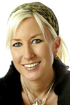 A smiling blonde woman wearing a leopard print headscarf and silver necklaces.