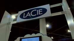 A large white sign with the word LACIE in a blue oval, mounted on a white frame under dark lighting.