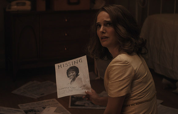 A woman in a light-colored dress sits on the floor holding a flyer that says MISSING with a photo of a girl.