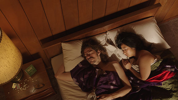 High angle view of a man and woman lying in bed under a purple blanket.