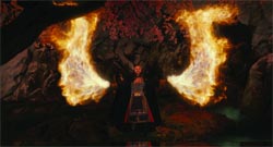A person in dark clothing stands with arms raised as two large plumes of fire erupt on either side.