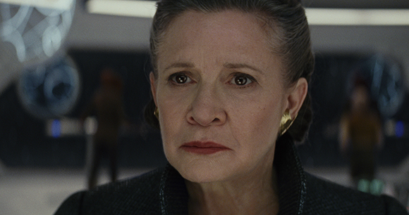 Close-up of an older woman with dark hair pulled back, looking forward with a somber expression.