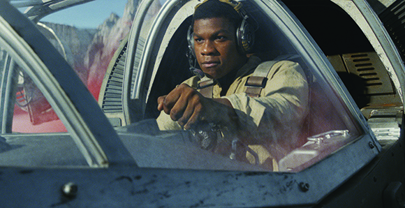 A pilot wearing headphones sits inside a spacecraft cockpit looking forward.