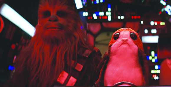 A tall, hairy Wookiee and a small, wide-eyed Porg sit in a dimly lit spaceship cockpit.