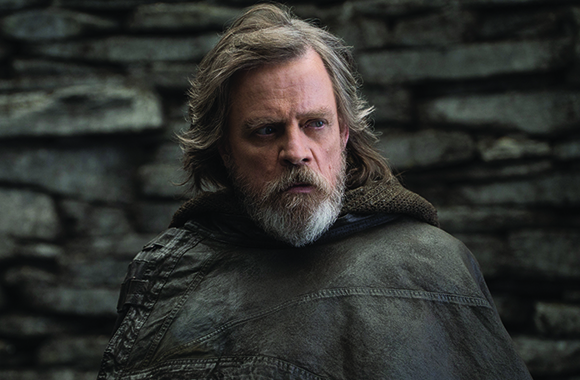 A man with long, wavy gray hair and a full gray beard wearing a dark textured cloak.