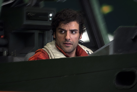 A man with dark curly hair looks intently out of a dark, mechanical cockpit.