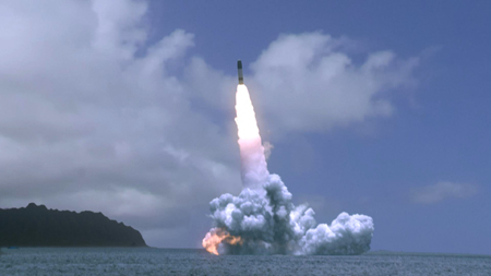 A missile ascends from the sea, leaving a bright white flame and a large cloud of white smoke.
