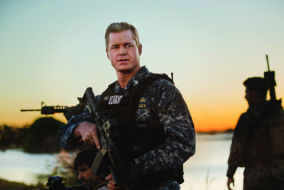 A man in blue digital camouflage military uniform looking over his shoulder.