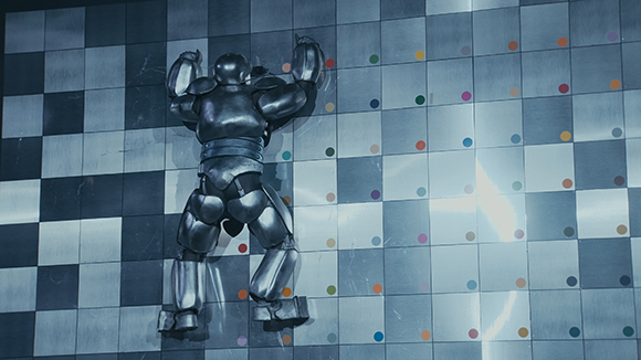 A silver metallic humanoid figure attached to a blue and white checkered wall with colorful dots.