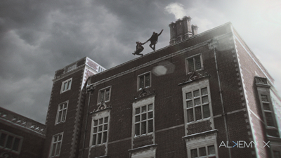 Two silhouettes jumping on the roof of a large brick building under a cloudy sky.