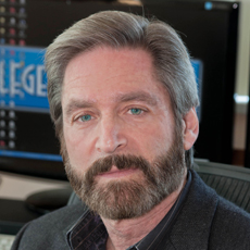 A man with graying hair and a full beard looking directly at the camera in an office setting.
