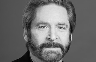 Black and white close-up portrait of a middle-aged man with a beard and light-colored eyes.