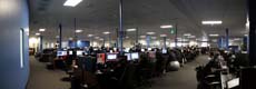 A wide view of a large office filled with rows of computer workstations and employees.