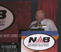A man in a light blue shirt speaks behind a podium featuring the NAB logo.