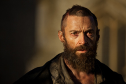 A bearded man with a cut on his forehead and a weary expression looking into the distance.