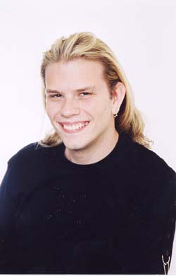 A smiling young man with long blonde hair wearing a black long-sleeved shirt against a white background.