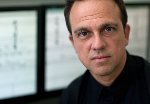 Close-up portrait of a man with dark hair and a black shirt looking directly at the camera.
