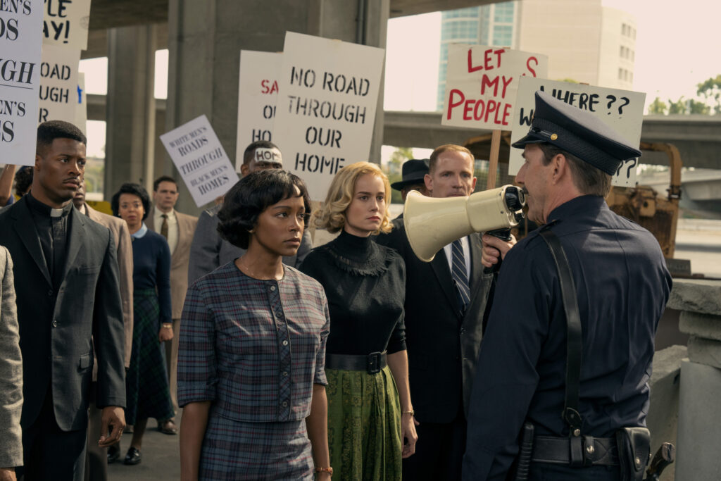 Protesters holding signs face a police officer holding a megaphone during a street demonstration.