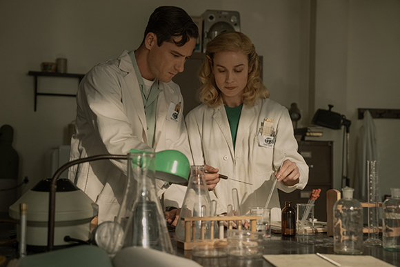 A man and a woman in white lab coats working with glassware in a dimly lit laboratory.