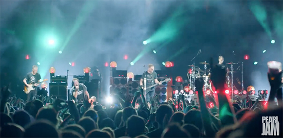 A rock band performs on a stage with green spotlights in front of a large crowd.