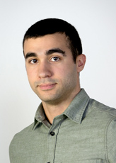 A man with short dark hair and dark eyes wearing a light green button-down shirt against a white background.