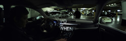 View from inside a dark car looking through the windshield at a parking garage with several vehicles.